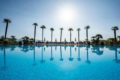 a large swimming pool with palm trees in the background at Onda Blu Resort in Manerba del Garda