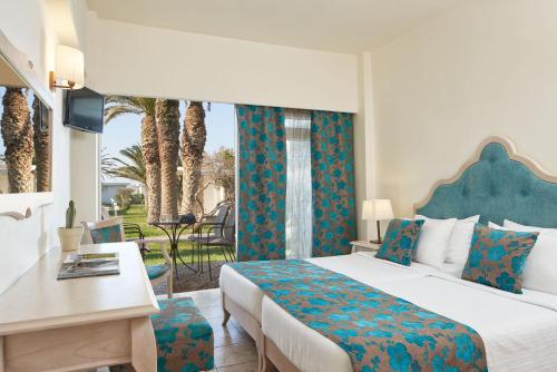 a bedroom with a bed and a desk and a window at Civitel Creta Beach in Amoudara Herakliou