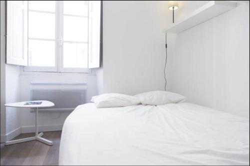 a white bedroom with a bed and a table at Quai bourgeois in Bordeaux
