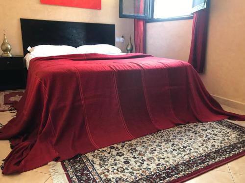 een bed met een rode deken op een tapijt bij Ali Appartement in Essaouira