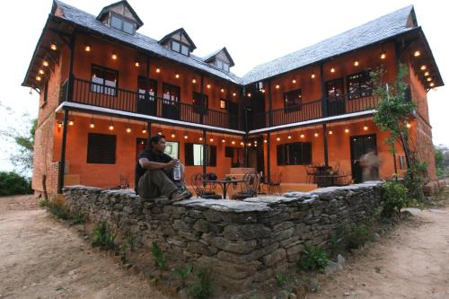 a man sitting on a stone wall in front of a building at Depche Village Resort in Bandīpur