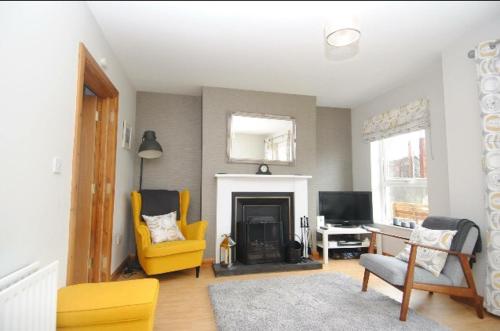 a living room with yellow chairs and a fireplace at Causeway Coastal Terrace Holiday Home portstewart in Portstewart