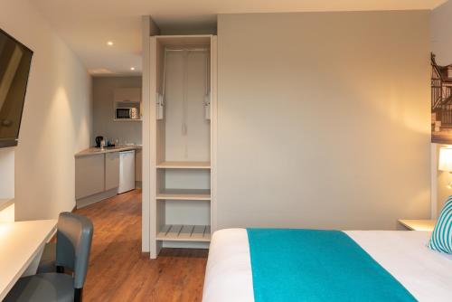 a bedroom with a bed and a desk and a kitchen at The Originals City, Hôtel Acadine, Pont-Audemer in Pont-Audemer