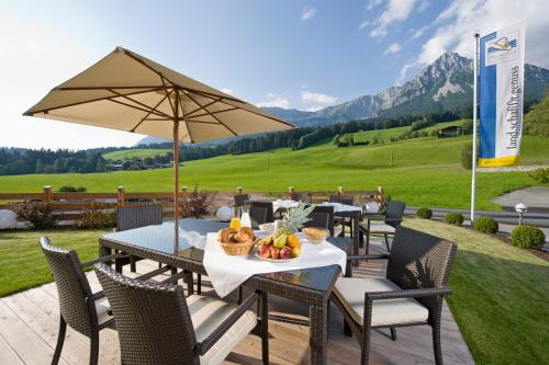 a patio with tables and chairs and an umbrella at Landhotel Föhrenhof Ellmau in Ellmau