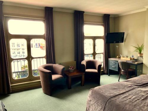 a hotel room with a bed and chairs and windows at Grand Cafe Hotel de Bourgondier in Bergen op Zoom
