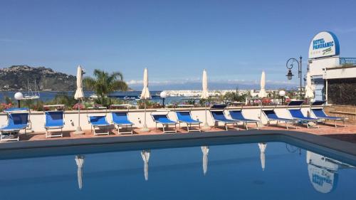 a row of blue and white lounge chairs next to a swimming pool at Hotel Panoramic in Giardini Naxos
