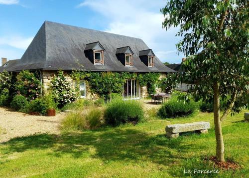 una casa con un techo negro con un banco delante en La Forcerie maison d'hôtes et spa, en Châtelais