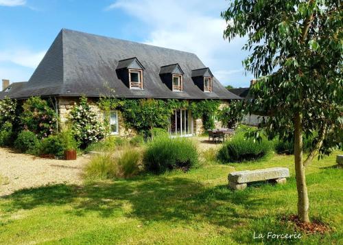 une maison avec un toit noir et un banc devant elle dans l'établissement La Forcerie maison d'hôtes et spa, à Châtelais
