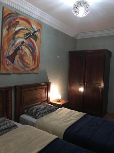 a bedroom with two beds and a painting on the wall at Wiss Appartement in Essaouira