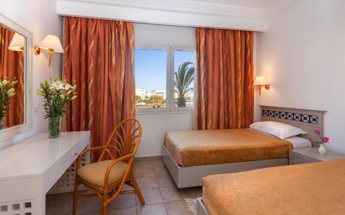 a hotel room with two beds and a desk and a window at Le Corail Appart'Hotel Yasmine Hammamet in Hammamet