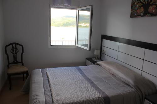 a bedroom with a bed and a window and a chair at Apartamento Corcubion Playa de Quenxe in Corcubión