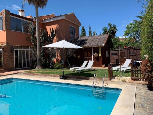 a swimming pool with an umbrella and chairs and a house at Chalet con piscina a 50 m de la playa . in Marbella