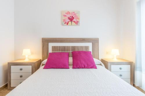 1 dormitorio con cama blanca y almohadas rosas en COMFORTABLE, CLOSE TO THE BEACH, POOL, NEW, PADDLE, en Rincón de la Victoria