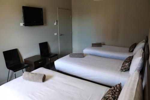 a room with three beds and a tv and a chair at Akuna Motor Inn and Apartments in Dubbo