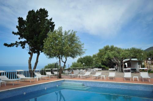 a swimming pool with white chairs and trees and the ocean at Residence Punta Cilento in Pisciotta