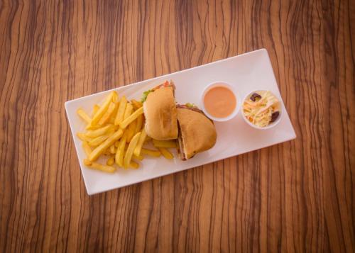 a white plate with a sandwich and fries and sauce at James Court Hotel & Luxury Apartments in Lekki