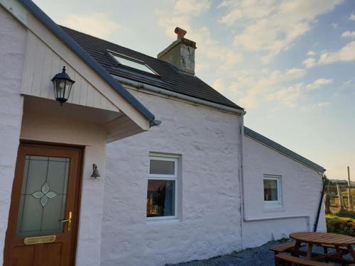 a white cottage with a wooden door and a picnic table at Arle Farmhouse in Tobermory