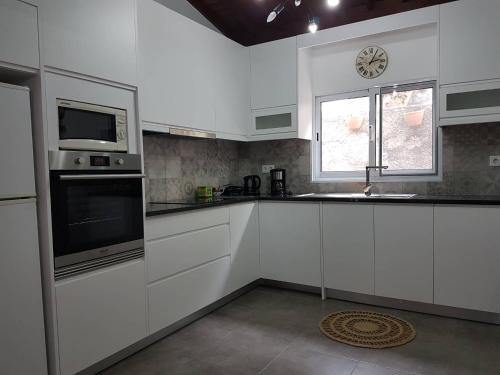 una cocina con armarios blancos y un reloj en la ventana en Join our relaxed house near the beach - Mosteiros en Mosteiros