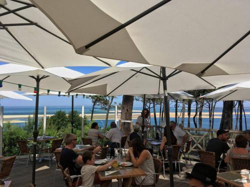 Un groupe de personnes assises à des tables sous des parapluies blancs dans l'établissement Maison familiale proche dune Pyla, plages, lac de Cazaux, sites de loisirs, à La Teste-de-Buch