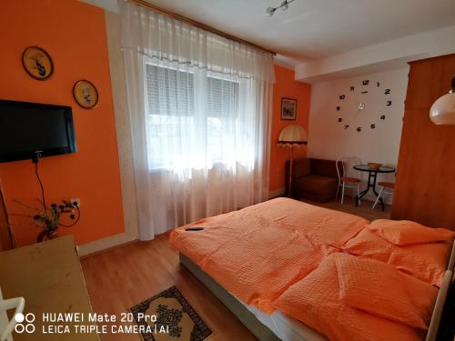 a bedroom with orange walls and a bed and a window at Paksy Apartman in Harkány