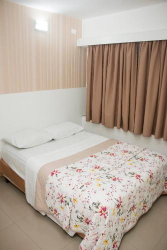 a bedroom with a bed with a floral blanket on it at Hotel Morada do Mar in Guarujá