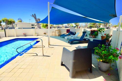 um pátio com um guarda-sol e cadeiras e uma piscina em Sunset Beach Holiday Park em Geraldton