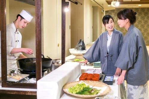 a couple of people standing in a kitchen preparing food at Hotel Shion in Morioka