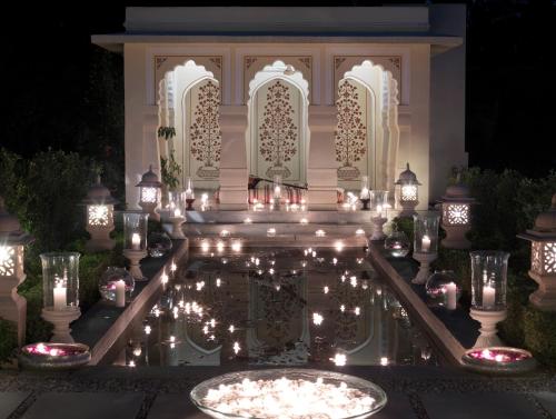 a garden with candles in the water at night at Rambagh Palace in Jaipur