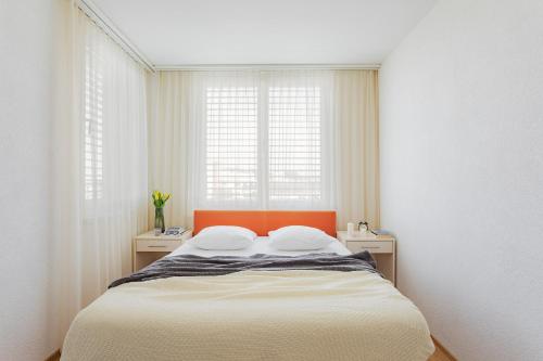 1 Schlafzimmer mit einem Bett mit einem orangefarbenen Kopfteil und 2 Fenstern in der Unterkunft Swiss Star Oerlikon Lodge - Self Check-In in Zürich