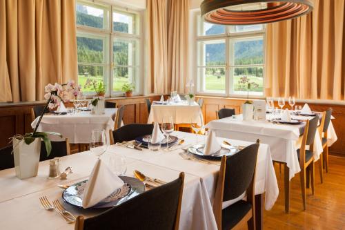 Hotel Tre Cime Sesto - Sexten في سيستو: مطعم بطاولات بيضاء وكراسي ونوافذ