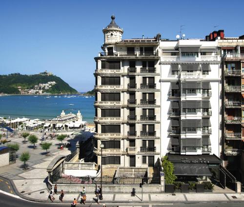 un grand bâtiment blanc avec une tour d'horloge à côté de l'océan dans l'établissement Hotel Niza, à Saint-Sébastien