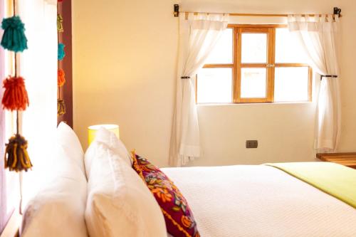 a bedroom with a bed with white pillows and a window at Casa de La Chola in Ollantaytambo