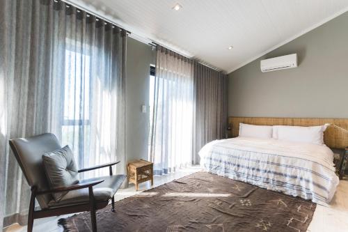 a bedroom with a bed and a chair and windows at The Gekko Lodge in Cape Town