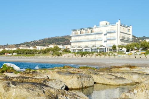 卡普多蘭多的住宿－Capo Nettuno Hotel，海滩上一座白色的大建筑,岩石