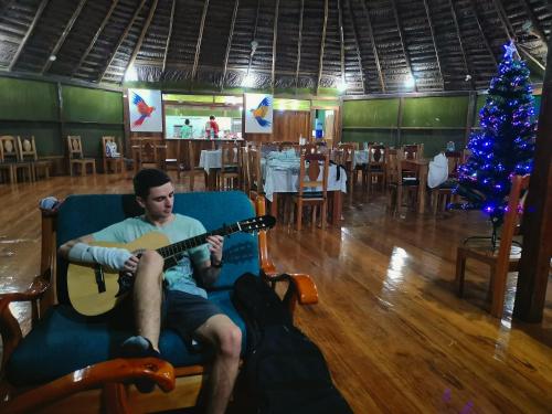 a man sitting in a chair playing a guitar next to a christmas tree at Grand Amazon Lodge and Tours - All Inclusive in Paraíso