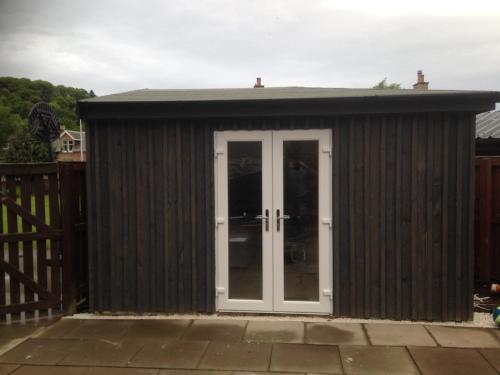 a large wooden shed with a white door at ensuite garden room in Inverness