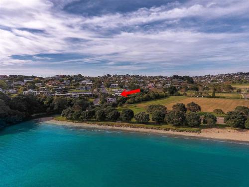 an aerial view of a beach with a red house at Stanmore Bay Beach House in Whangaparaoa
