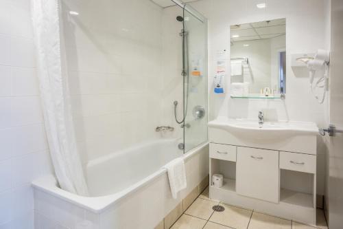 a white bathroom with a tub and a sink at President Hotel Auckland in Auckland