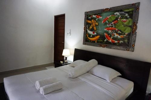 a bedroom with a white bed with a painting on the wall at Ary Guest House in Canggu