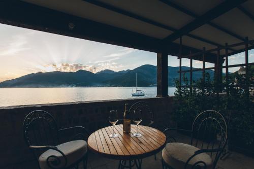 een houten tafel en stoelen met wijnglazen op een balkon bij Eco Hotel Carrubba in Tivat