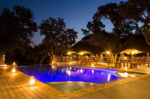 a swimming pool at night with tables and umbrellas at Vuyani River Lodge in Hoedspruit