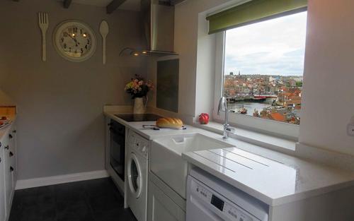 a kitchen with a clock on the wall and a window at Ropery Cottage - Cyanacottages in Whitby