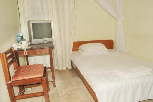 Habitación pequeña con cama y escritorio con TV. en Scroll Inn Hotel en Kampala