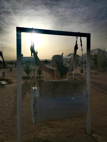 a woman sitting in a swing with the sun in the background at Berber Camp in Merzouga