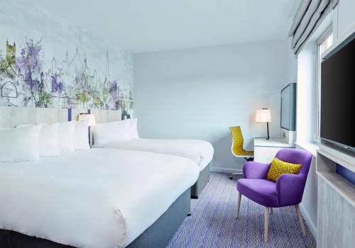 a hotel room with a large bed and a purple chair at Leonardo Hotel Exeter in Exeter