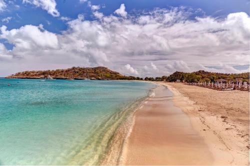 a beach with blue water and an island in the background at Royalton Antigua, An Autograph Collection All-Inclusive Resort in Five Islands Village