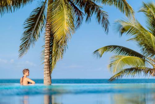 a boy standing under a palm tree in the water at Almond Beach Resort at Jaguar Reef in Hopkins