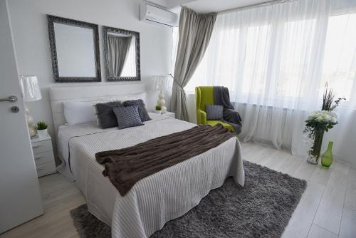 a white bedroom with a bed and a green chair at Metropole Apartments Old Town in Bucharest