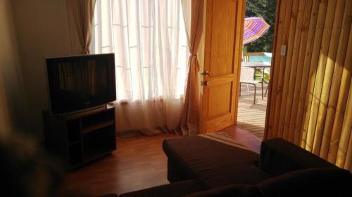 a living room with a television and a door to a patio at Refugios Olmue Santa Teresa in El Maqui