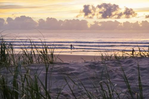 a person walking on the beach at sunset at San Marino by the Sea Apartments in Marcoola